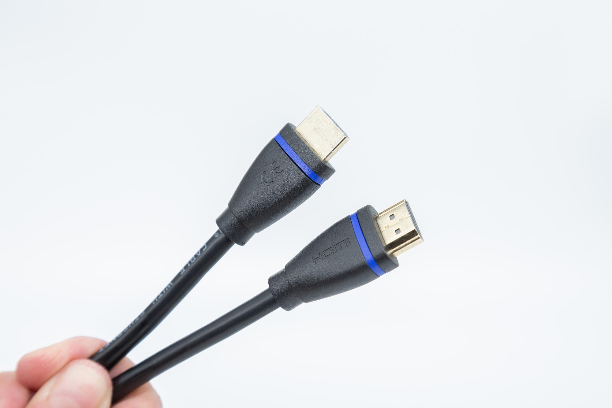 Zwei schwarze HDMI-Kabel mit goldfarbenen Steckern werden vor weißem Hintergrund gehalten.