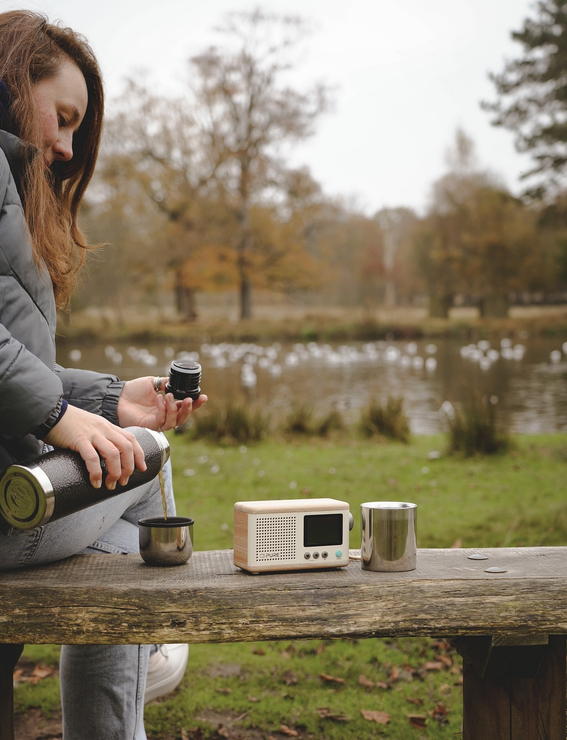 Kobieta nalewa płyn z termosu do kubka obok radia.