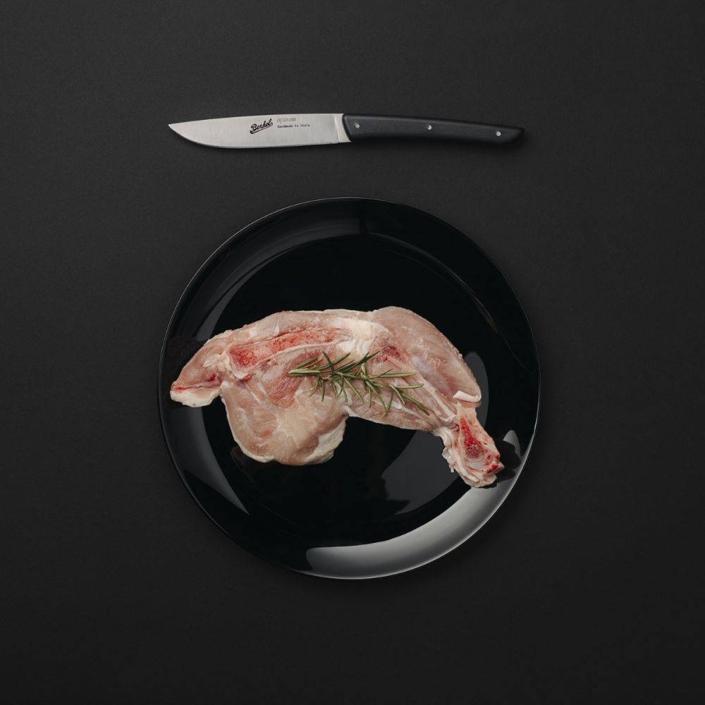 Black plate with raw meat and rosemary. Knife on top. Dark background.