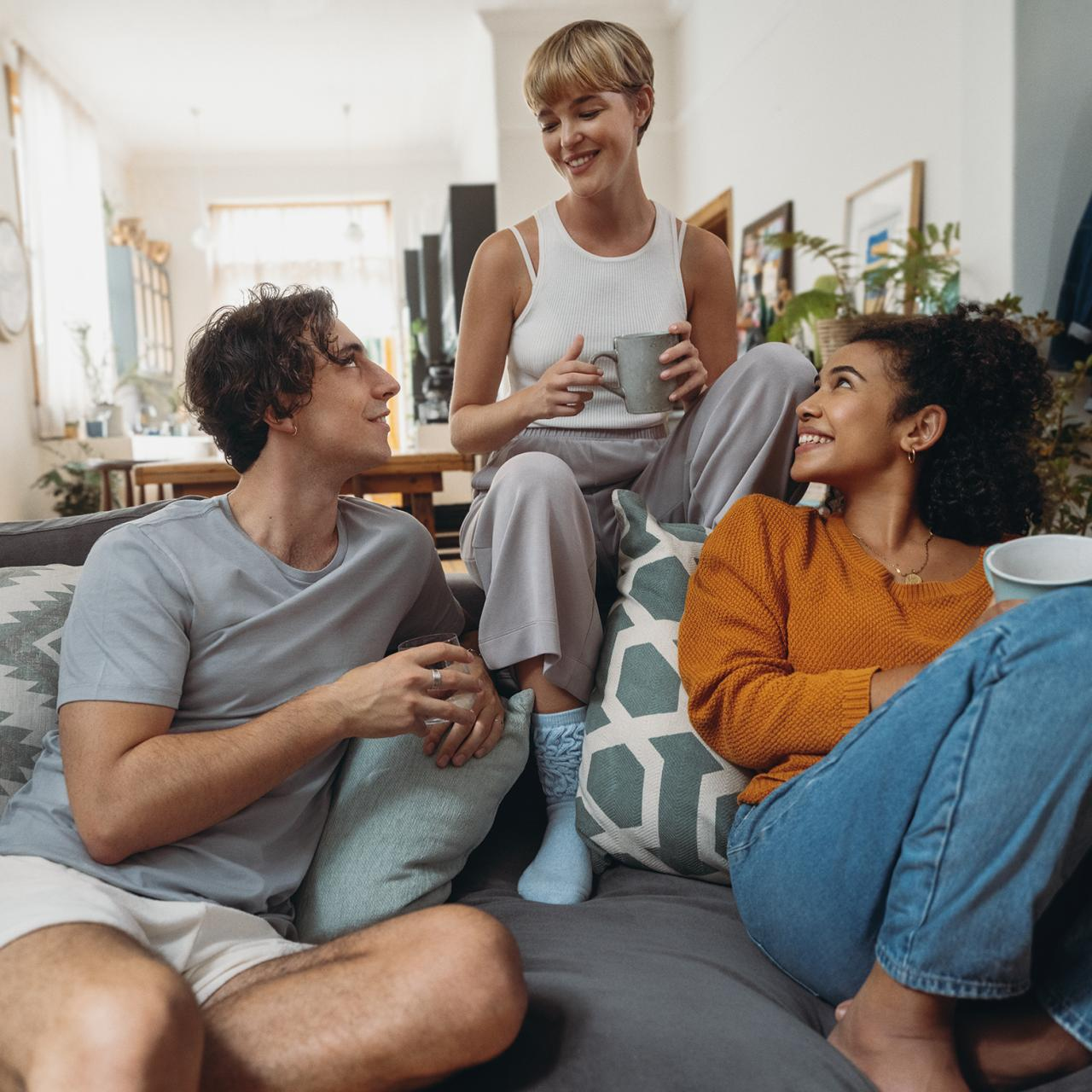 Trzy osoby na kanapie, dwie patrzą na siebie, jedna trzyma kubek.