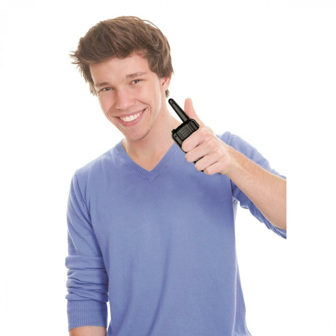 Młody mężczyzna trzymający krótkofalówkę i pokazujący kciuk w górę. Białe tło.