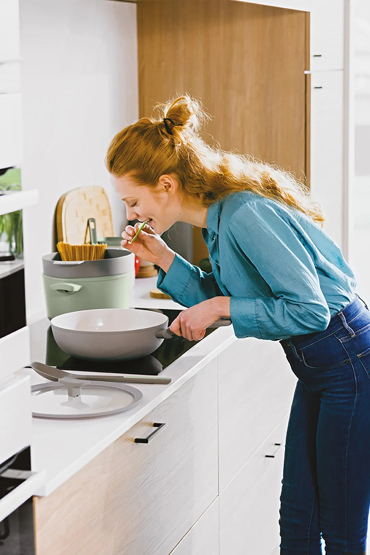 Woman smelling food from a pan on a stove.