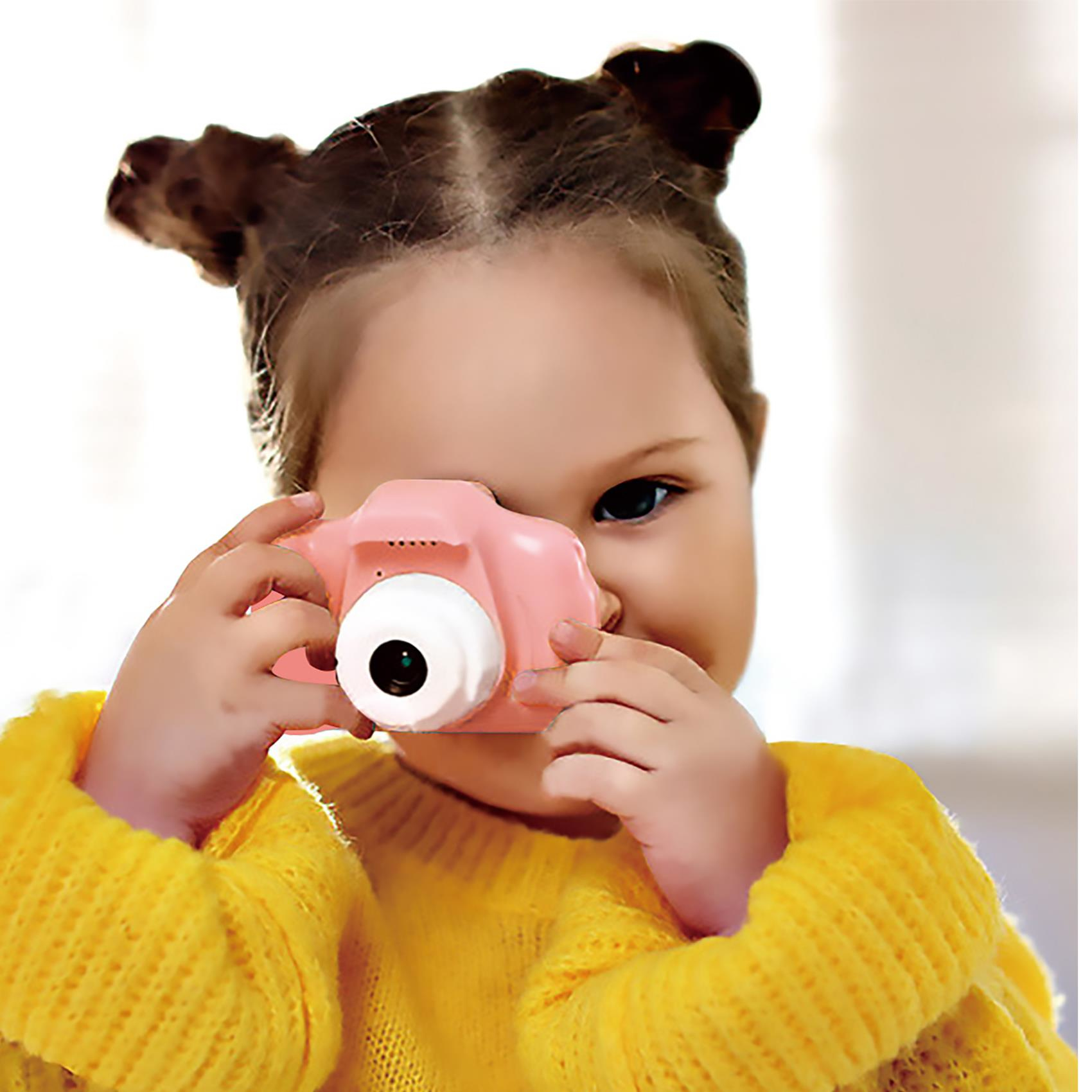 Una niña pequeña con cabello castaño sosteniendo una cámara rosa, sonriendo a la cámara.