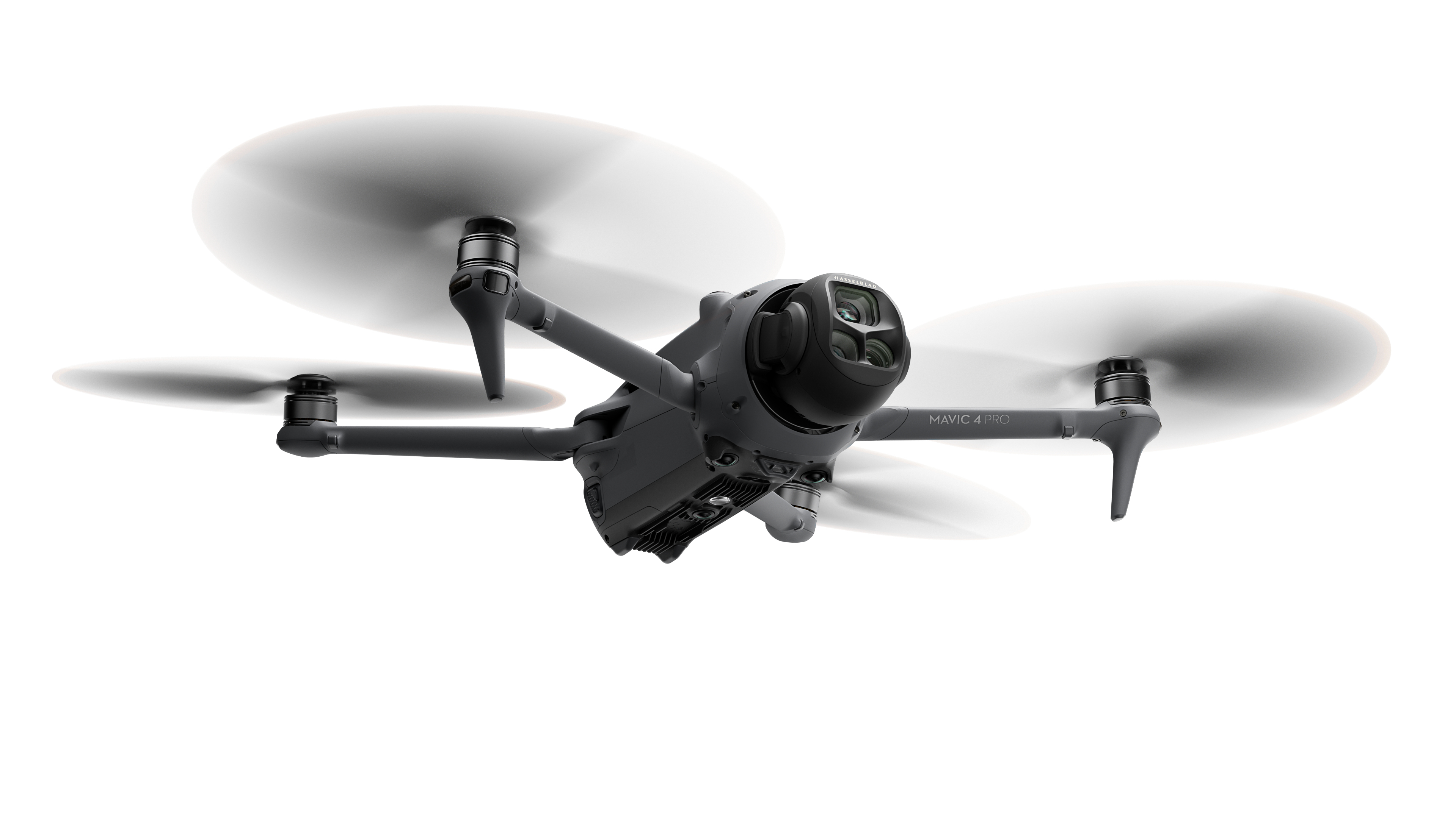 Szary dron z czterema śmigłami, skierowany do przodu. Białe tło.