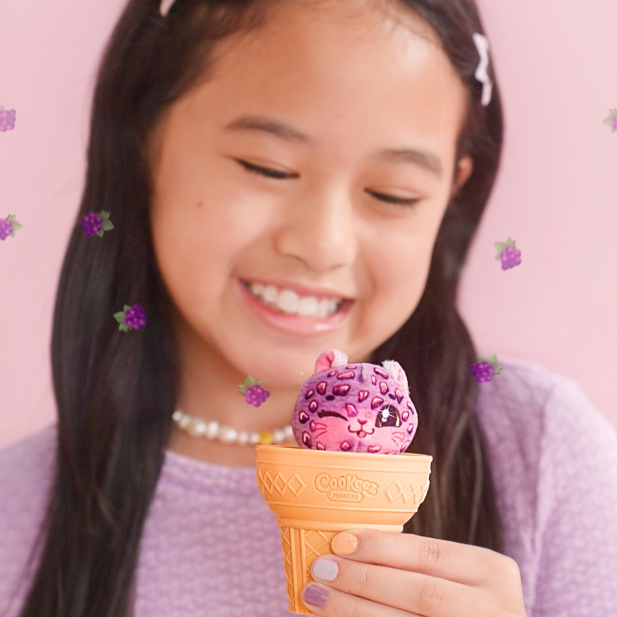 Niña sonriendo, sosteniendo un juguete Cookeez Yum Yumz en un cono de helado, colores morado y rosa.