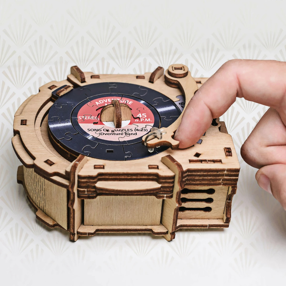 Un carillon in legno con un disco puzzle. Una mano gira la manovella della scatola.