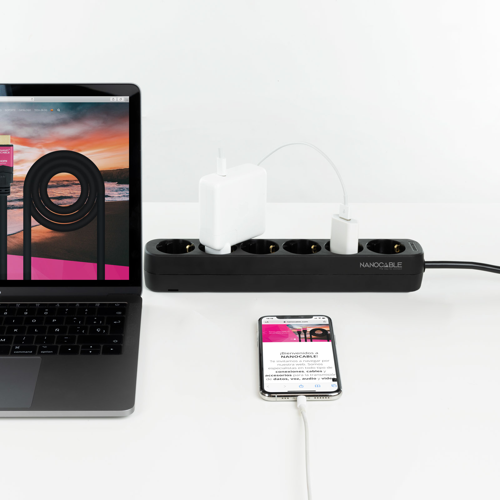 Laptop, telefoon en stekkerdoos op een wit oppervlak. Kabels en opladers zijn aangesloten.