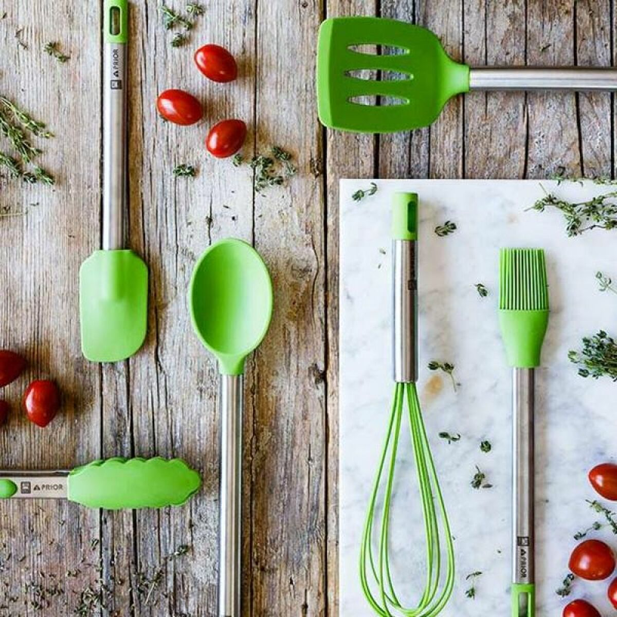 Kitchen utensils on a wooden surface. Includes spatulas, a whisk, and tomatoes.