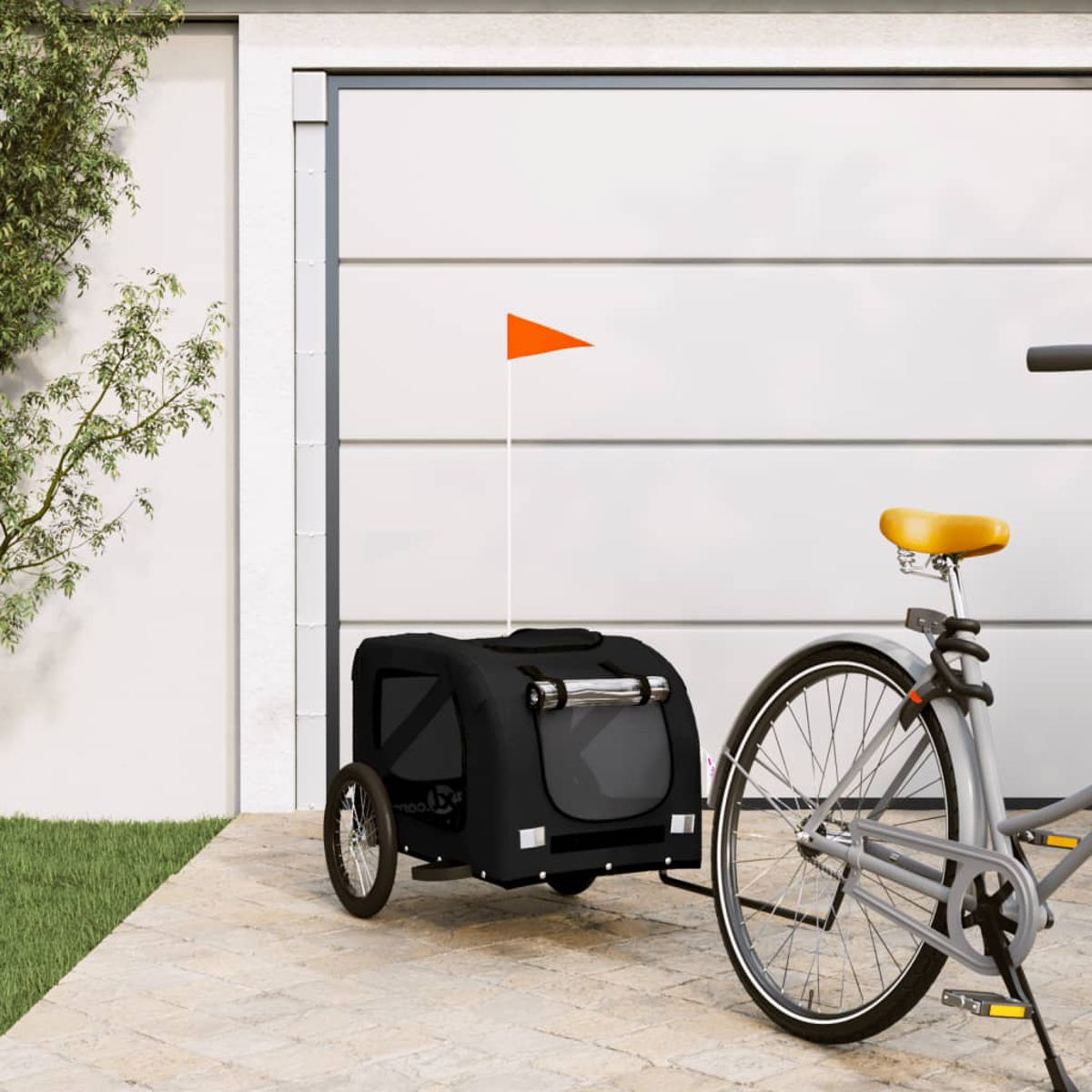 Ein schwarzer Fahrradanhänger mit einer orangefarbenen Fahne an einem Fahrrad, geparkt auf einer Terrasse.