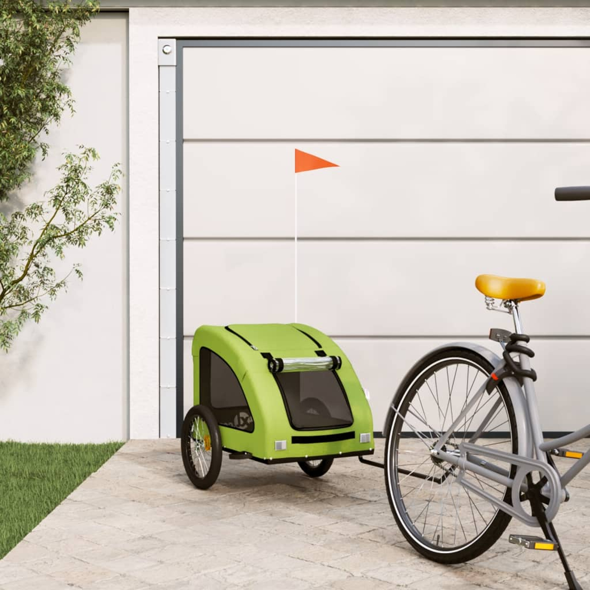 Ein grüner Fahrradanhänger mit einer orangefarbenen Fahne an einem Fahrrad, geparkt auf einer Terrasse.