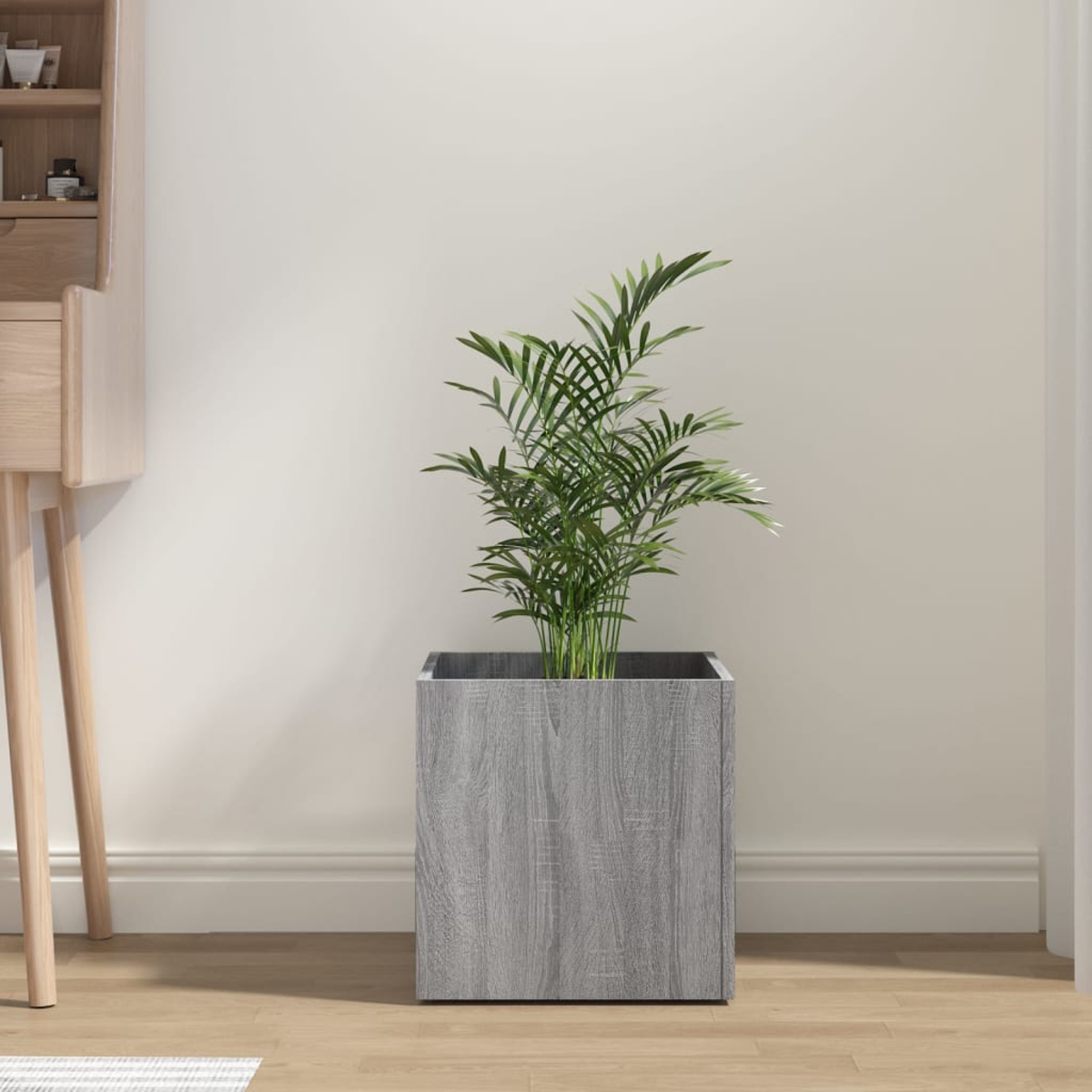 Ein grauer Holzpflanzer mit einer grünen Pflanze darin. Beige Wand im Hintergrund.