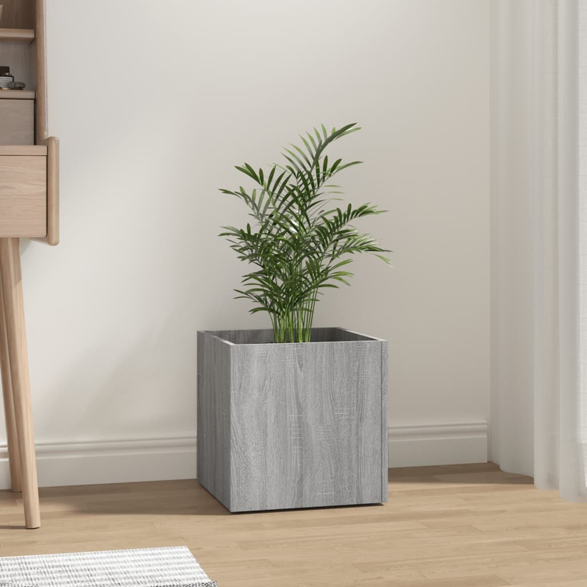 Ein würfelförmiger Pflanzkübel mit Grünzeug gefüllt. In einem Raum, auf einem Holzboden.