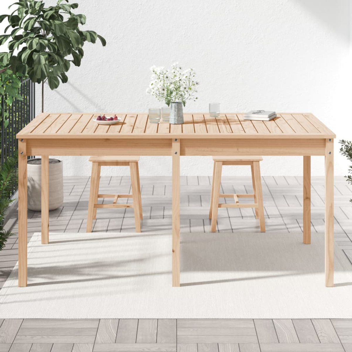 Ein Holztisch mit Hockern und einem Teppich. Blumen und Gläser stehen auf dem Tisch.
