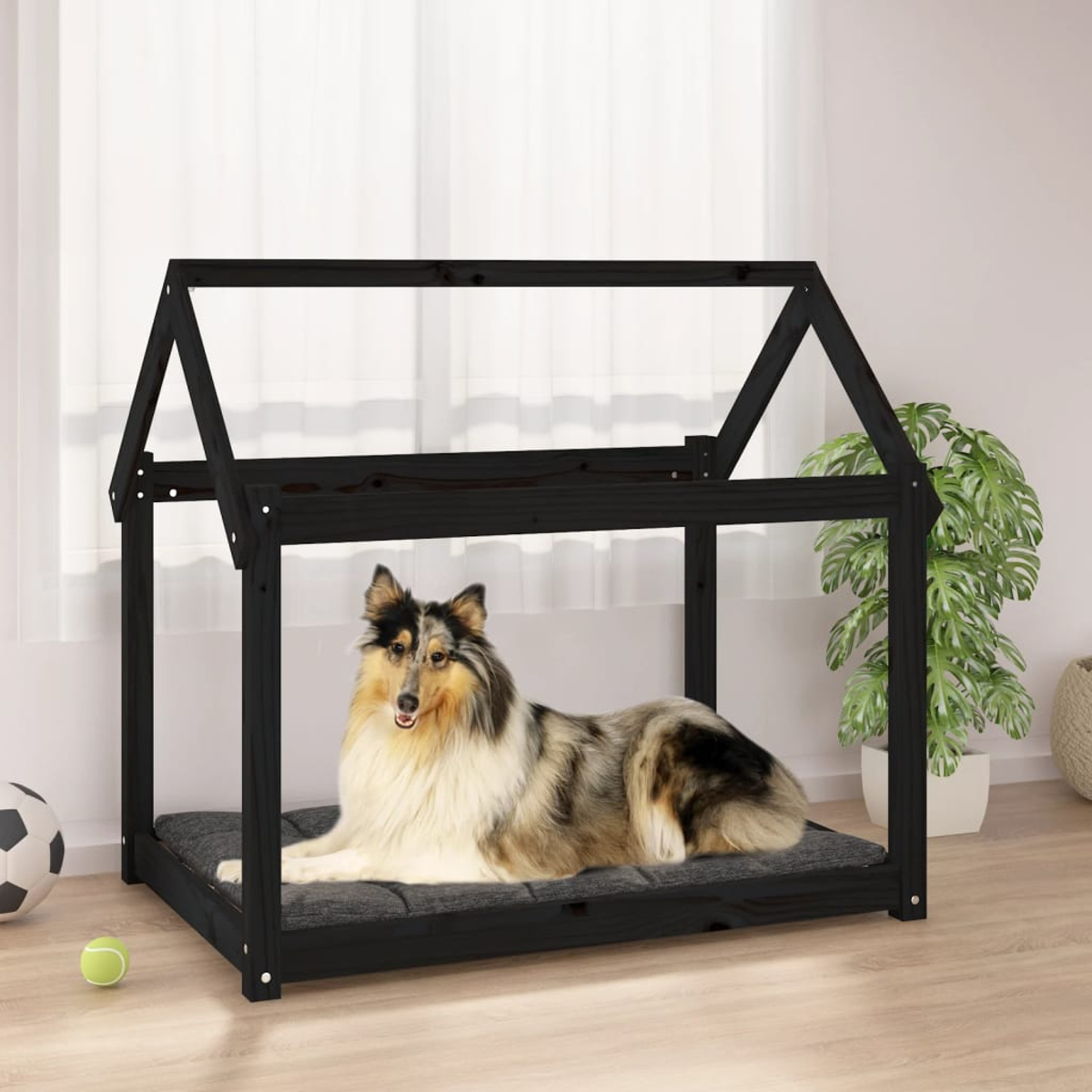 Hundebett mit Hund darin, in einem schwarzen, hausförmigen Holzrahmen. Ein Ball und ein Spielzeug sind vorhanden.