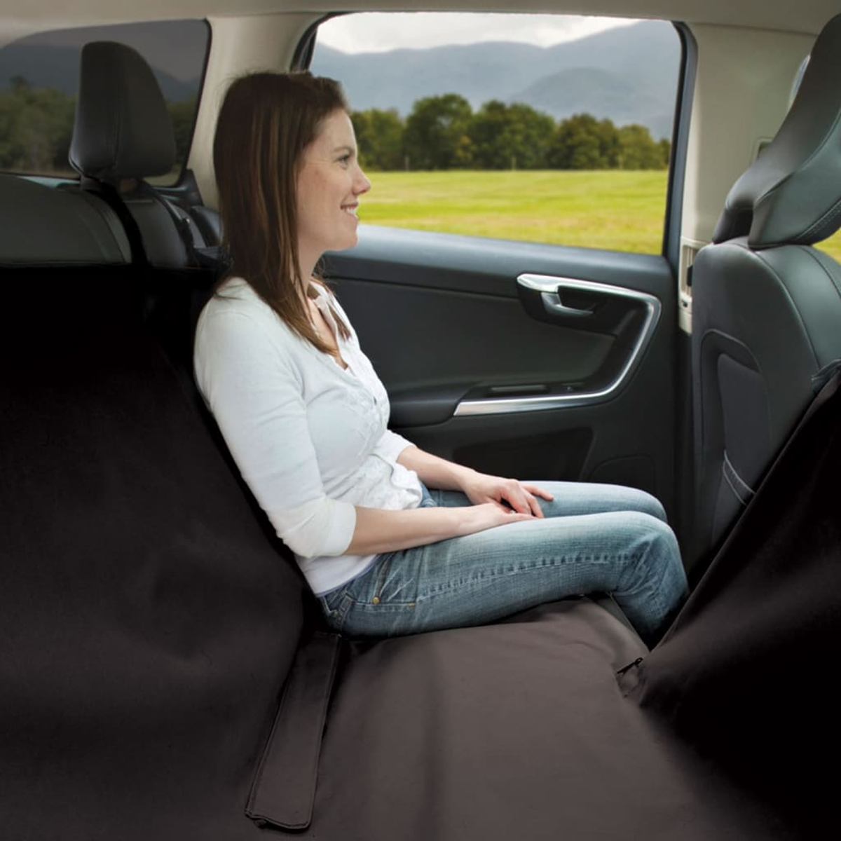 Eine Frau in einem Auto sitzt auf einem schwarzen Sitzbezug, mit grüner Landschaft im Hintergrund.