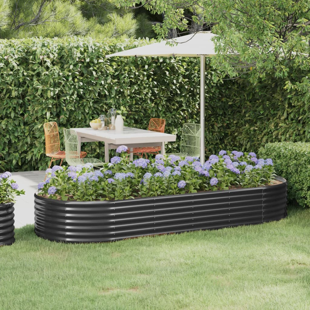 Ein schwarzes, erhöhtes Metall-Gartenbeet mit lila Blumen steht in einem Garten mit Tisch.