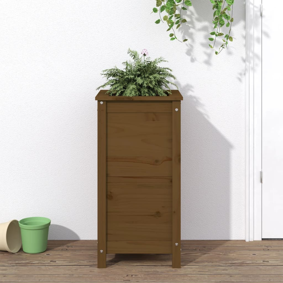 Eine braune Holzpflanzkasten, mit Pflanze darin, vor einer weißen Wand.