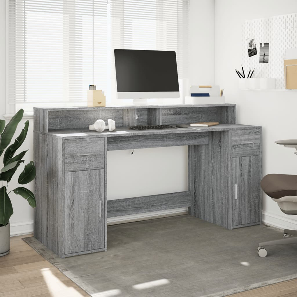 Grauer Holzschreibtisch mit Computer, Schubladen und Schränken. Im Hintergrund ein Fenster.