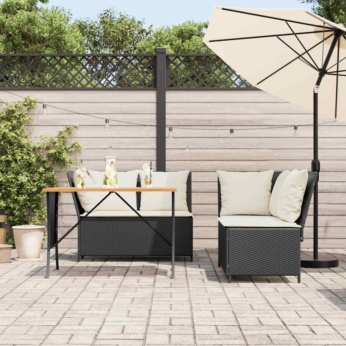 Patio all'aperto con mobili in rattan, ombrellone e luci a corda. Recinto in legno sullo sfondo.