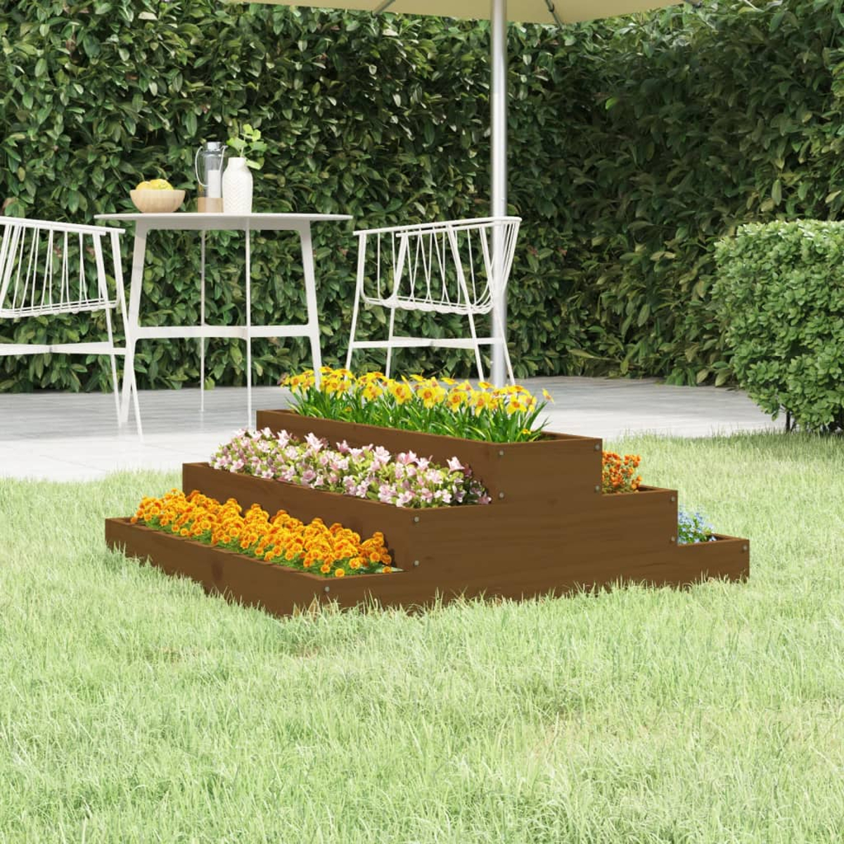 Holz-Blumenbeet mit bunten Blumen auf Rasen, Tisch und Stühle im Hintergrund.
