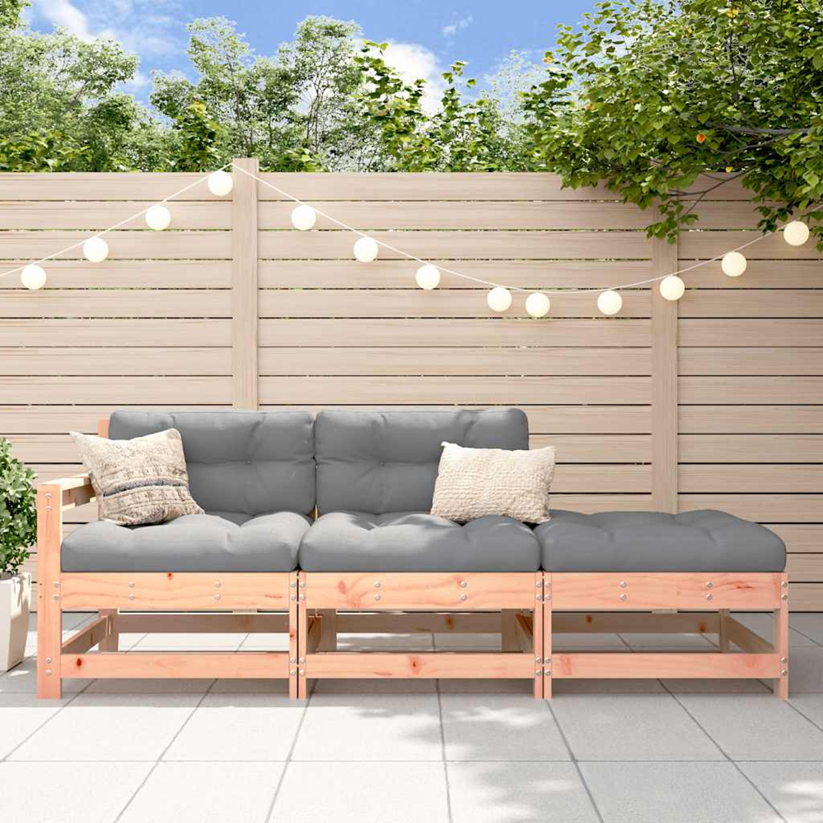 Graues Sofa mit Kissen auf Holzrahmen, auf Terrasse. Lichterkette und Zaun im Hintergrund.