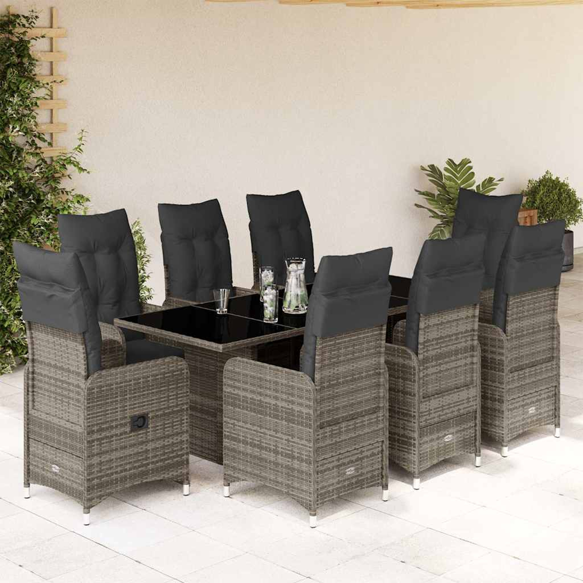 Tavolo e sedie in rattan su patio, cuscini neri, vetro e piante visibili.