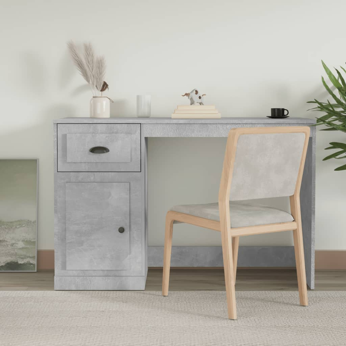 Grauer Schreibtisch mit Schublade und Schrank. Ein Stuhl, Pflanzen und Deko daneben. Weiße Wand.