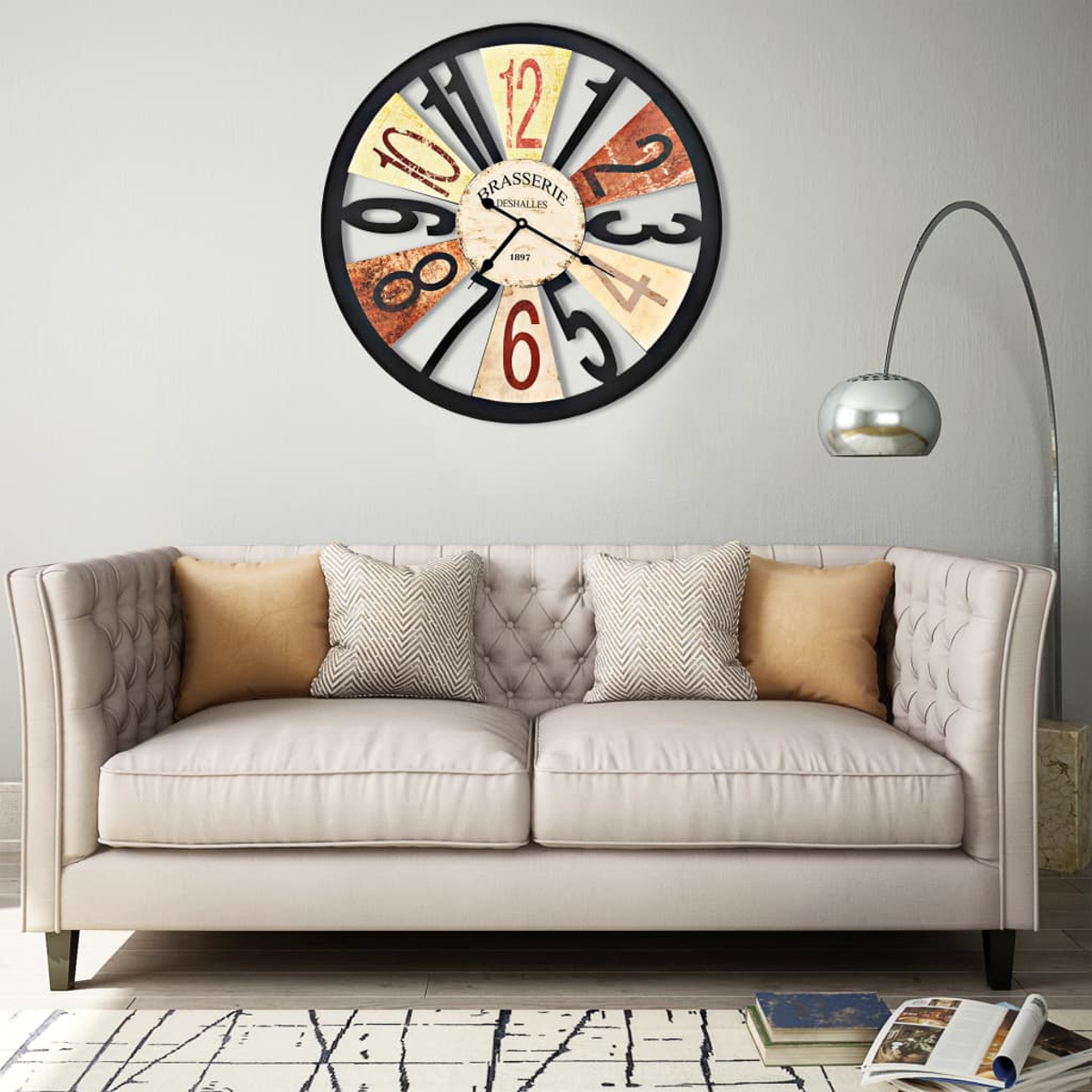 Eine Wanduhr hängt über einem Sofa mit Kissen, eine Stehlampe steht links.