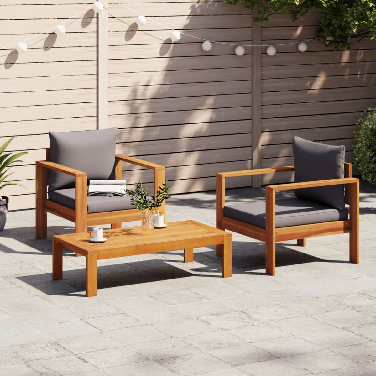 Set da patio con due poltrone in legno, un tavolino e uno sfondo in legno con luci.