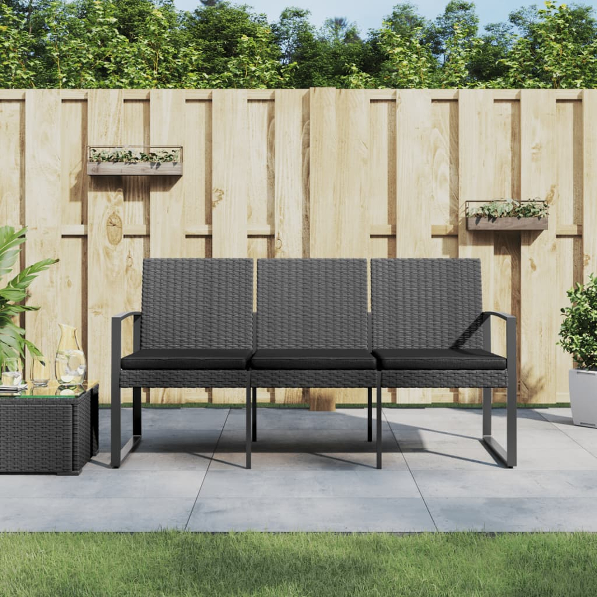 Graues Outdoor-Sofa aus Korbgeflecht mit schwarzen Kissen. Auf einer Terrasse.