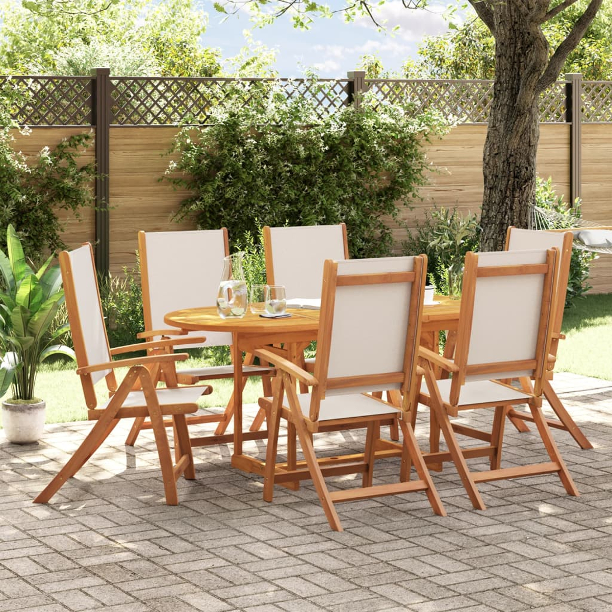Set da pranzo all'aperto con tavolo in legno, sei sedie e bicchieri. Piante e alberi verdi sullo sfondo.