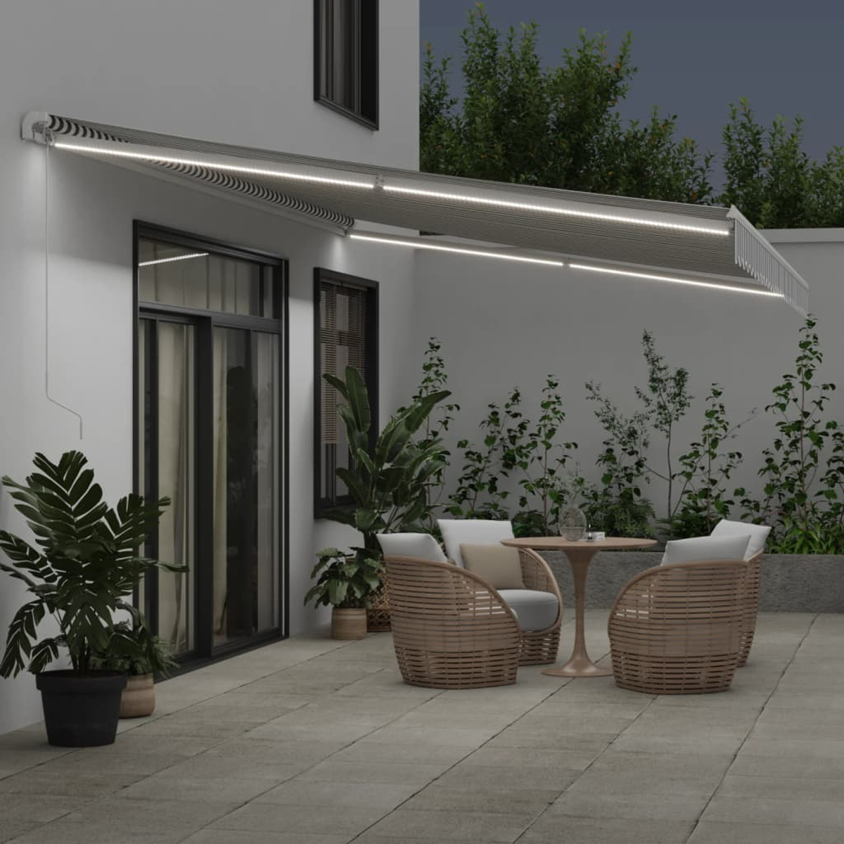 Hausfassade bei Nacht mit eingeschalteten Markisenlichtern, Tisch, Stühlen und Pflanzen.