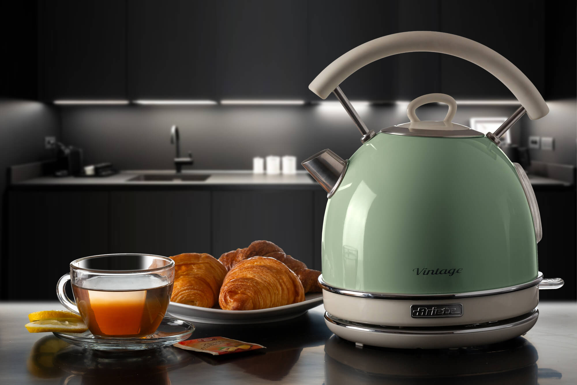 Een turquoise waterkoker op een tafel met croissants en een kopje thee voor een keuken.