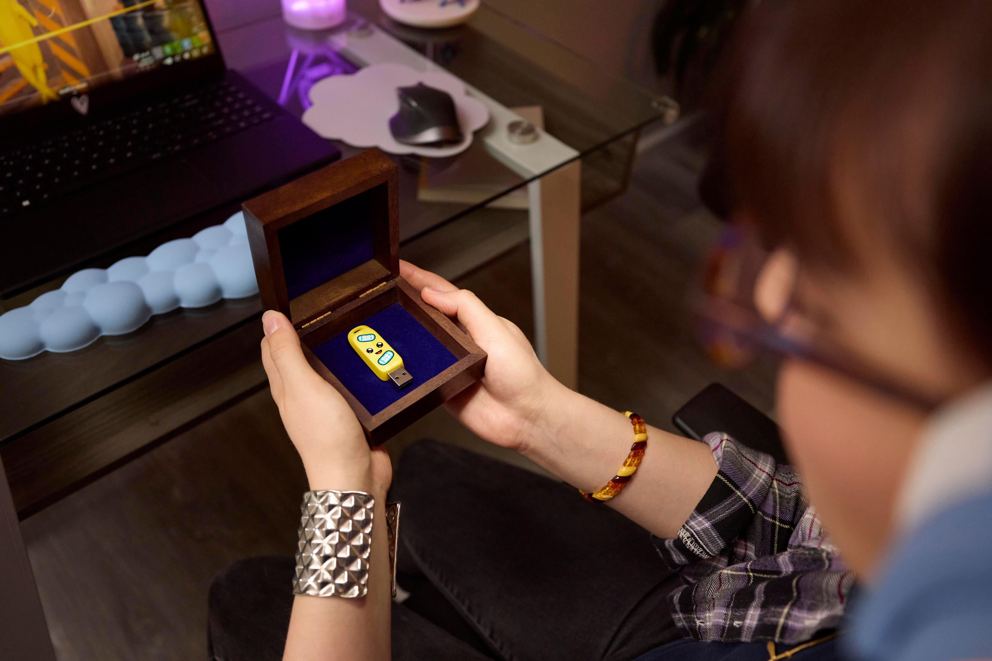 Osoba trzymająca żółty pendrive w drewnianym pudełku.