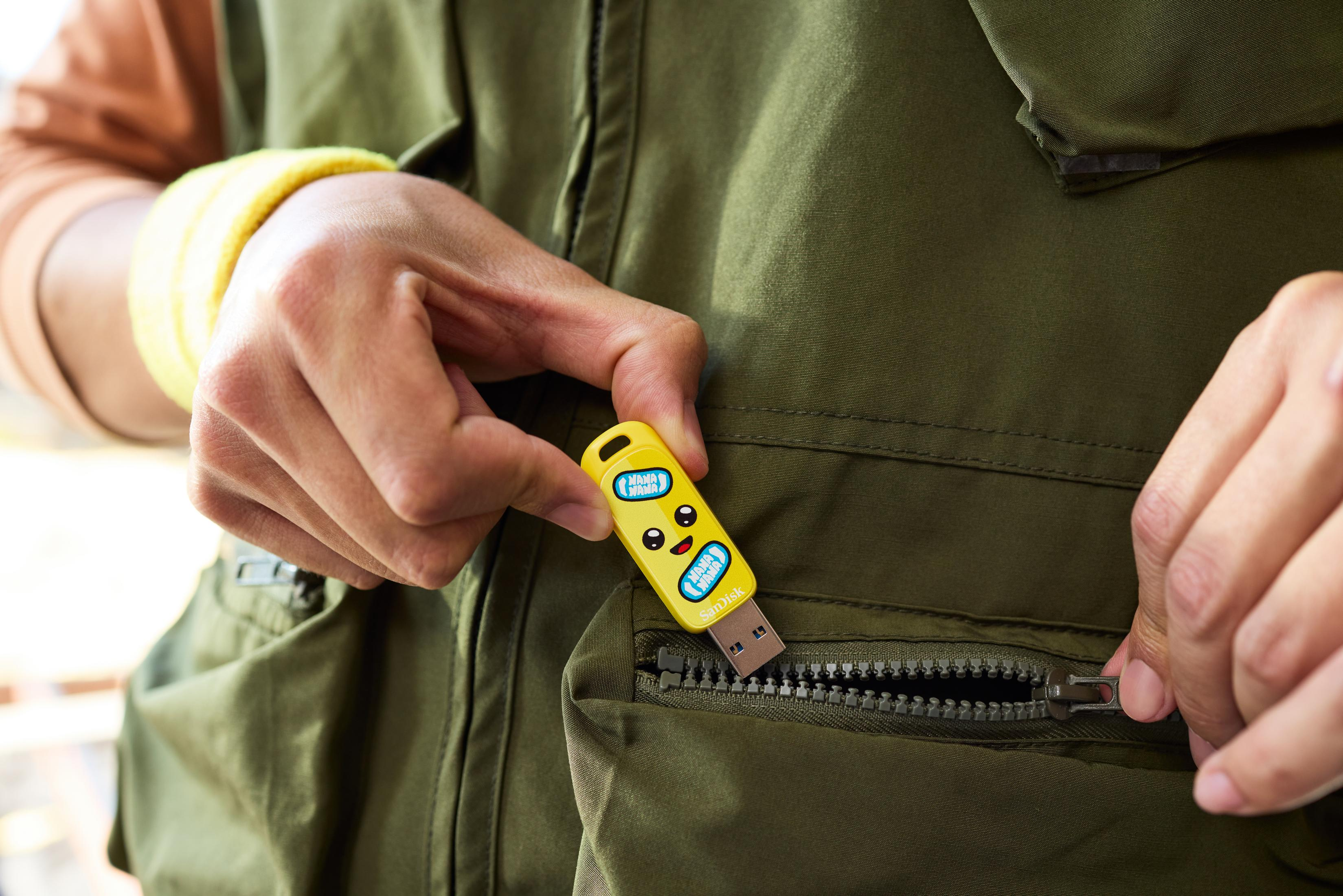 Ręka osoby wkładająca żółty pendrive do kieszeni.