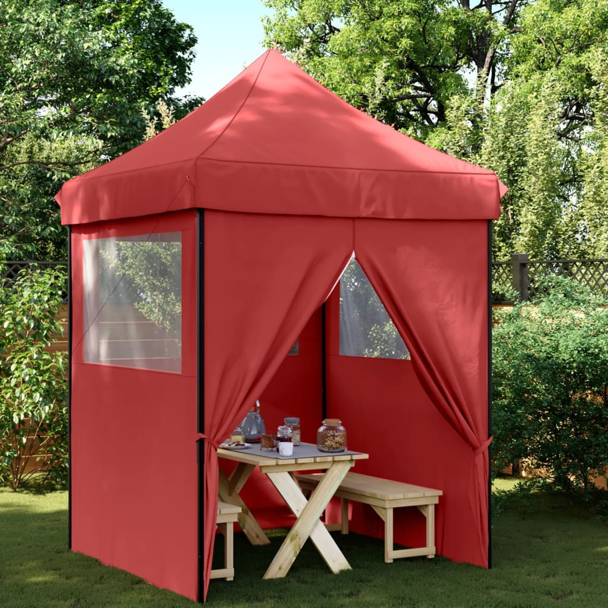 Rotes Pop-up-Zelt im Garten, mit Tisch, Bänken und Bäumen sichtbar.