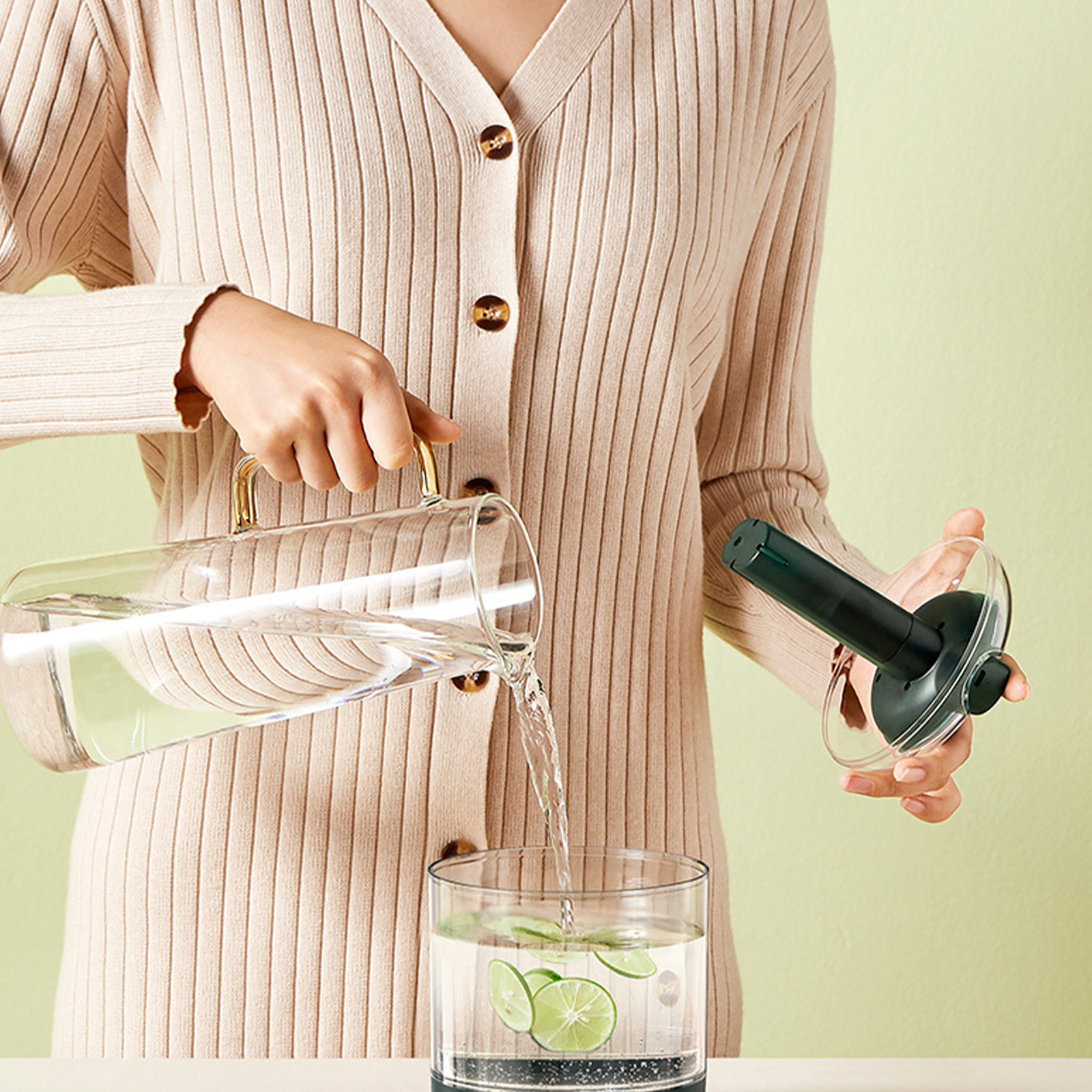 Frau gießt Wasser aus einer Glaskanne in ein Glas mit Limettenscheiben.