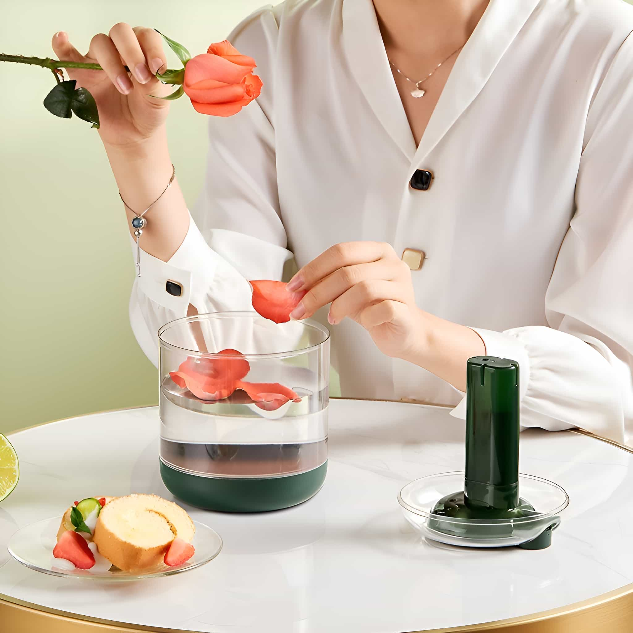 Frau legt Rosenblatt ins Wasserglas, Kuchen und Spender auf dem Tisch.