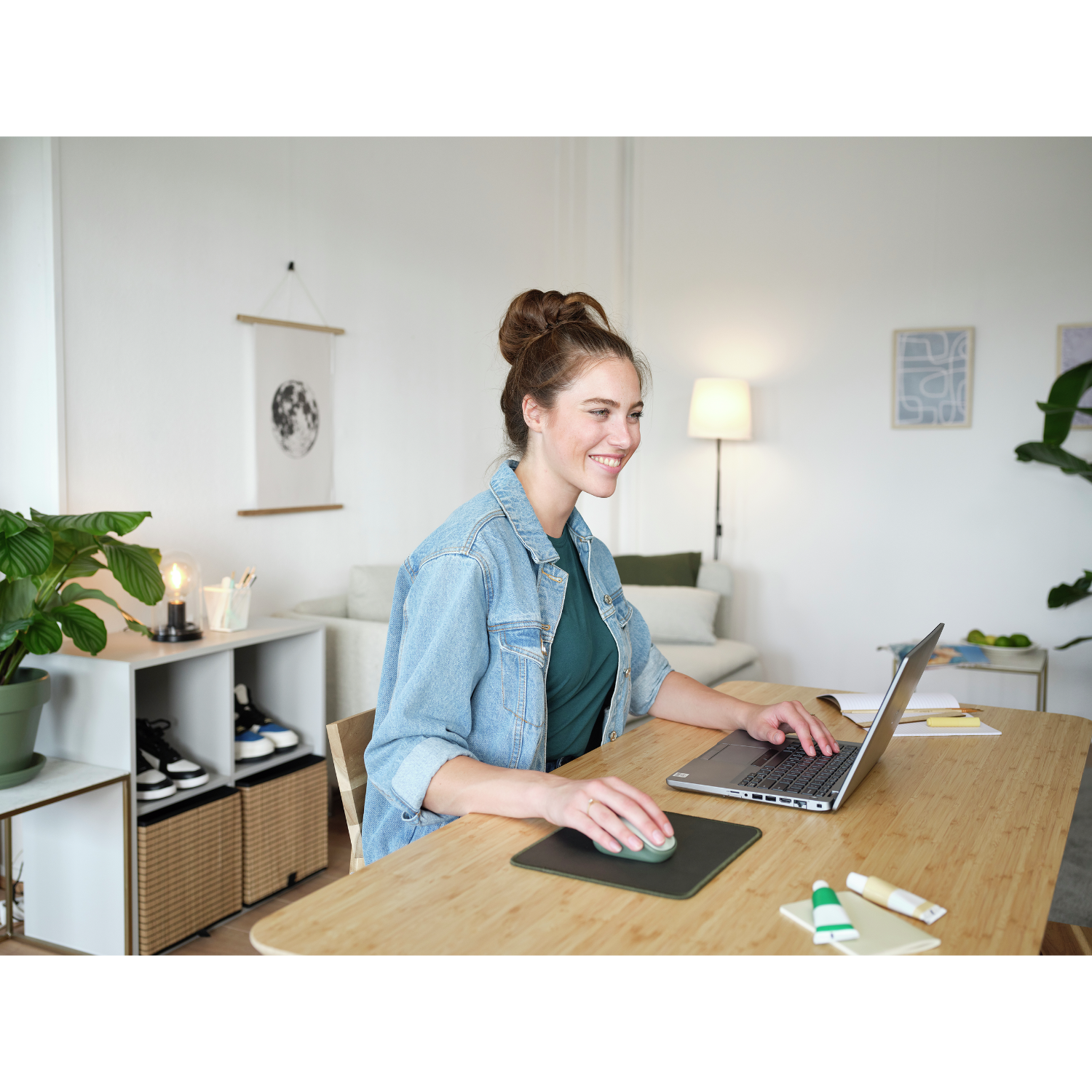 Une femme sourit devant un ordinateur portable sur un bureau, avec un tapis de souris vert et d'autres objets.