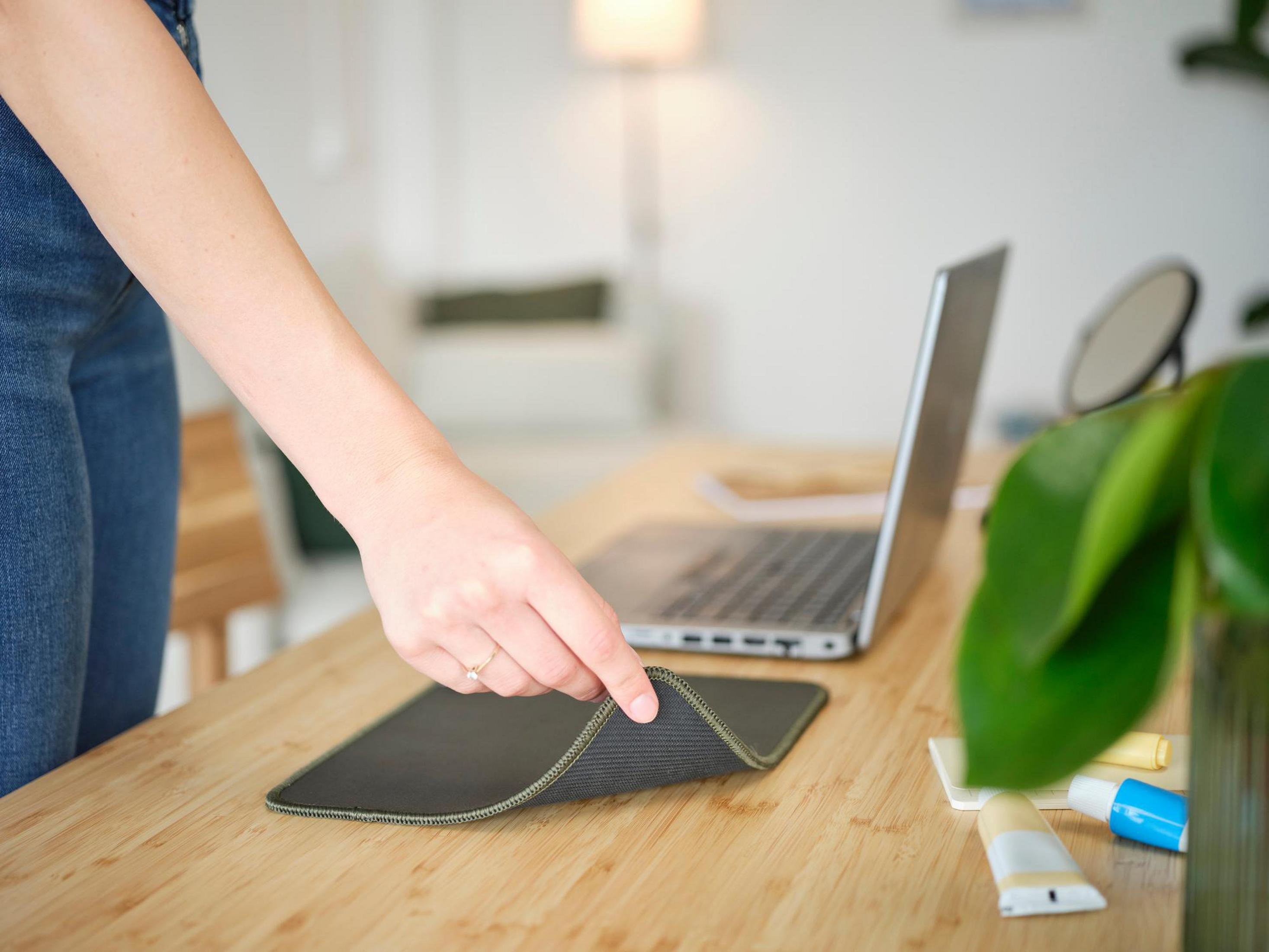 Main plaçant un tapis de souris vert sur un bureau en bois avec un ordinateur portable et d'autres objets.