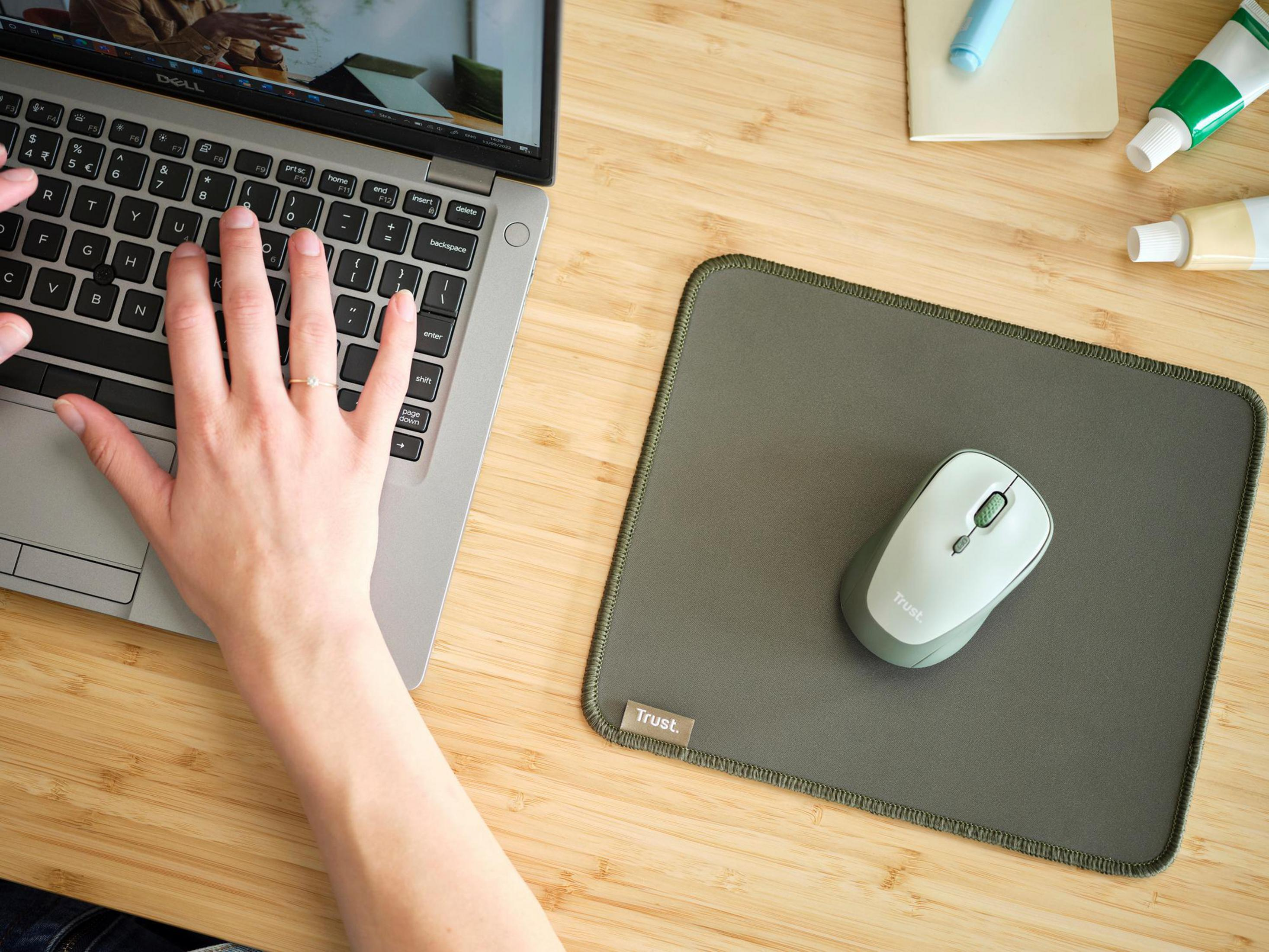 Une main sur un clavier, une souris et un tapis de souris, et un ordinateur portable sur un bureau en bois.