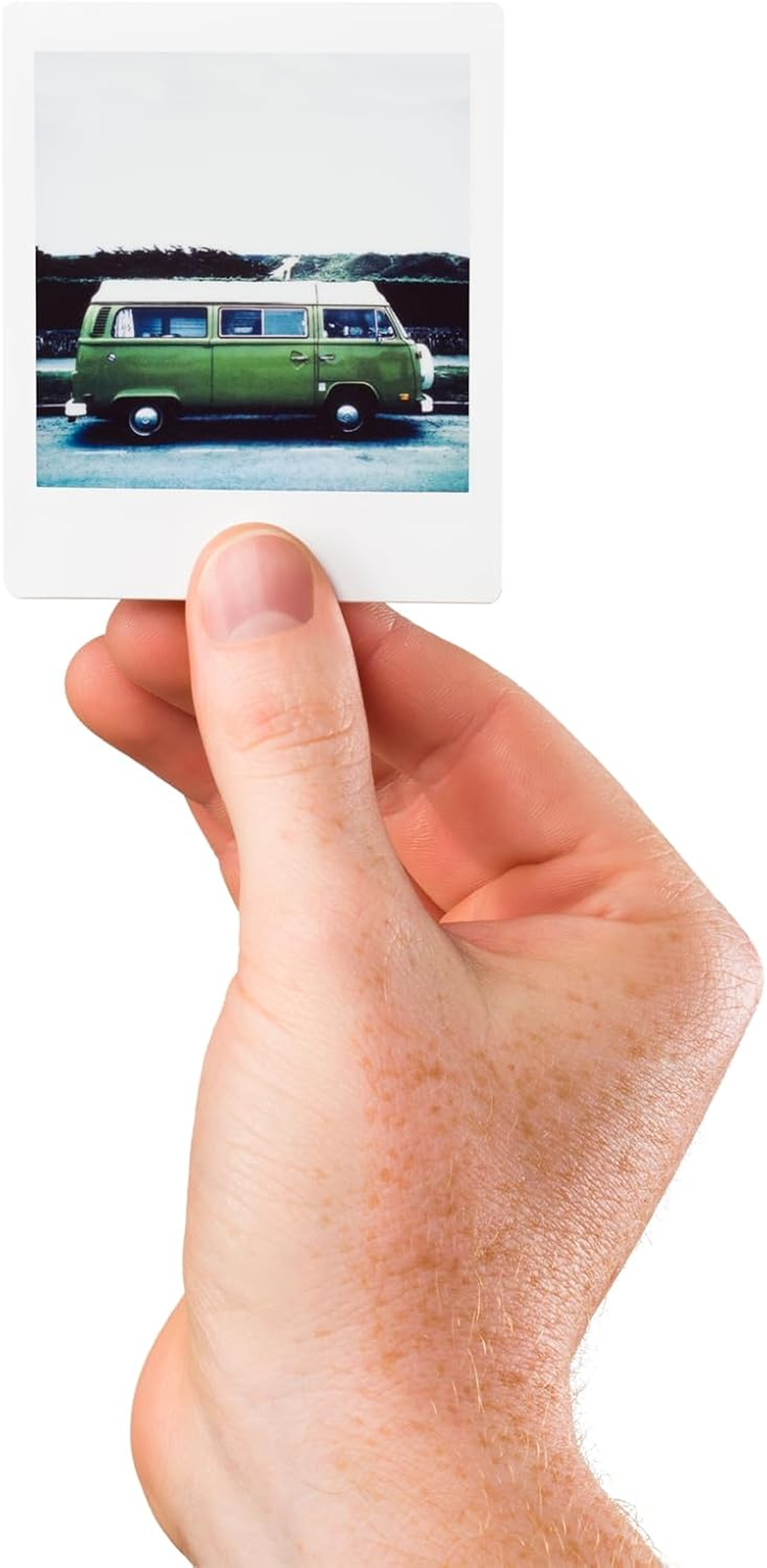Een hand die een polaroidfoto vasthoudt van een groene VW-bus op een weg. De achtergrond is een blauwe lucht.