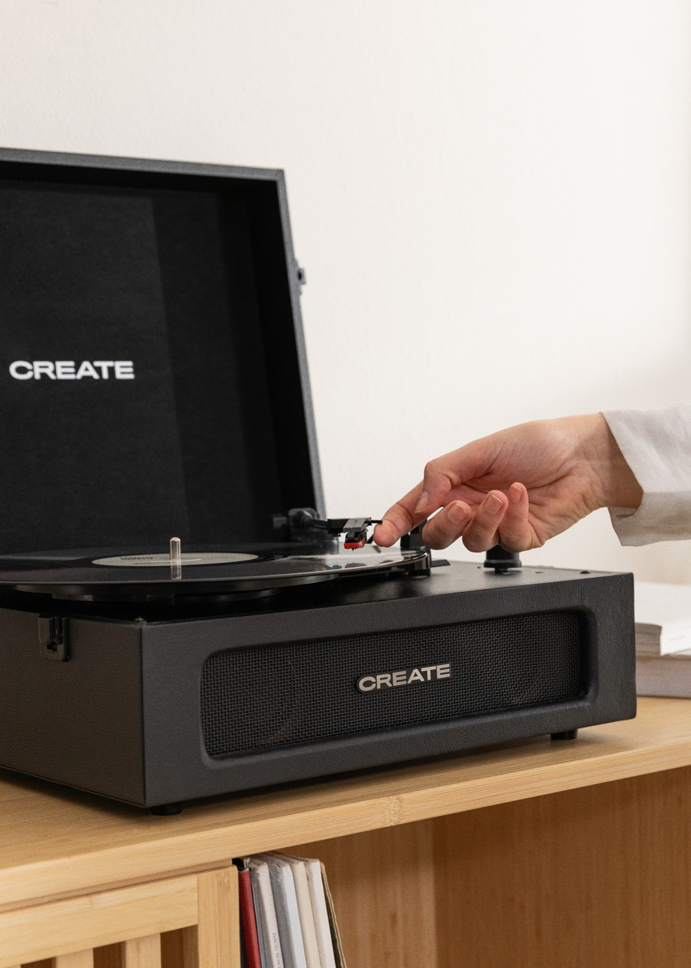 Un tocadiscos negro con una mano ajustando la aguja. La palabra CREATE está en la tapa.