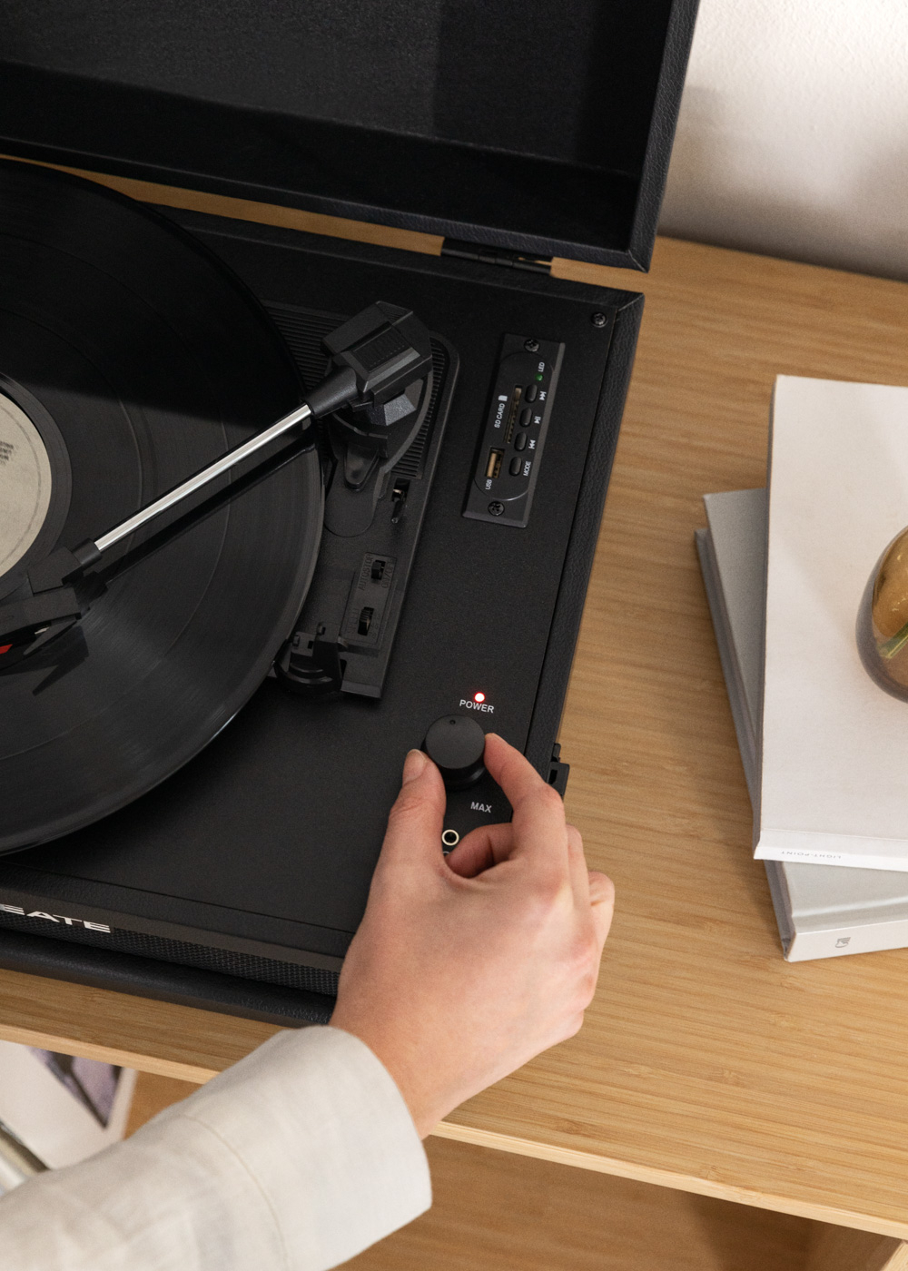 Una persona está girando la perilla de volumen de un tocadiscos negro, sobre un mueble de madera.