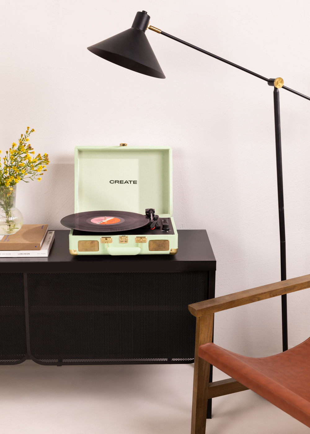 Un tocadiscos verde sobre un mueble negro. Una lámpara y una silla están cerca. CREATE es visible.
