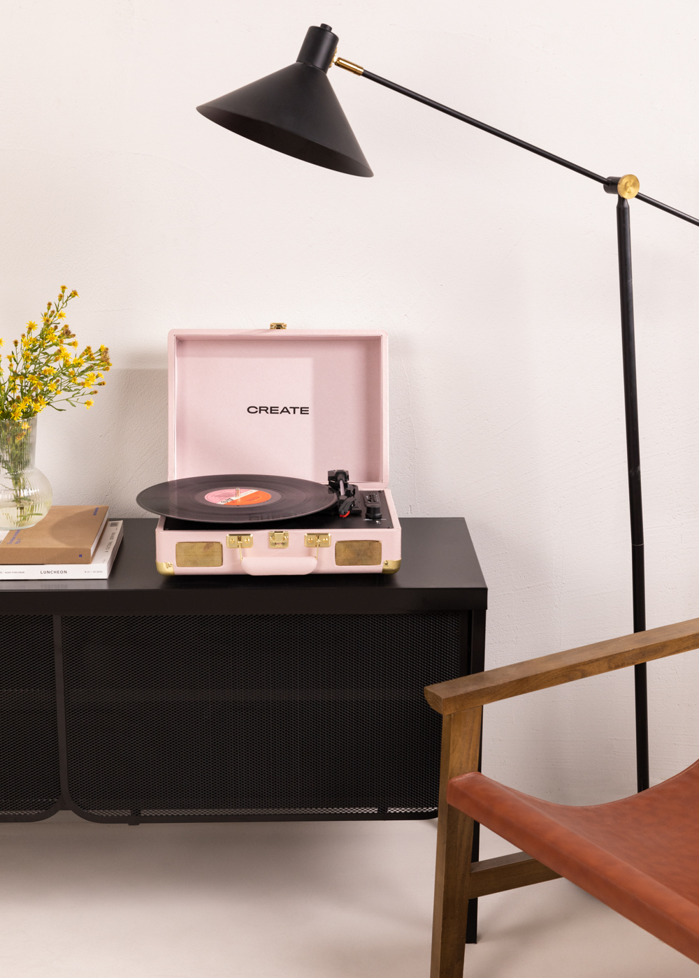 Un tocadiscos rosa sobre un mueble negro. Una lámpara y una silla están cerca. CREATE es visible.