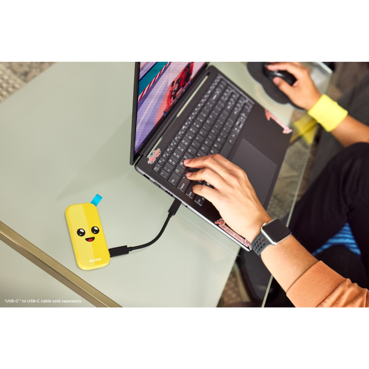 Osoba korzystająca z laptopa z żółtym zewnętrznym dyskiem twardym podłączonym do szklanego stołu.