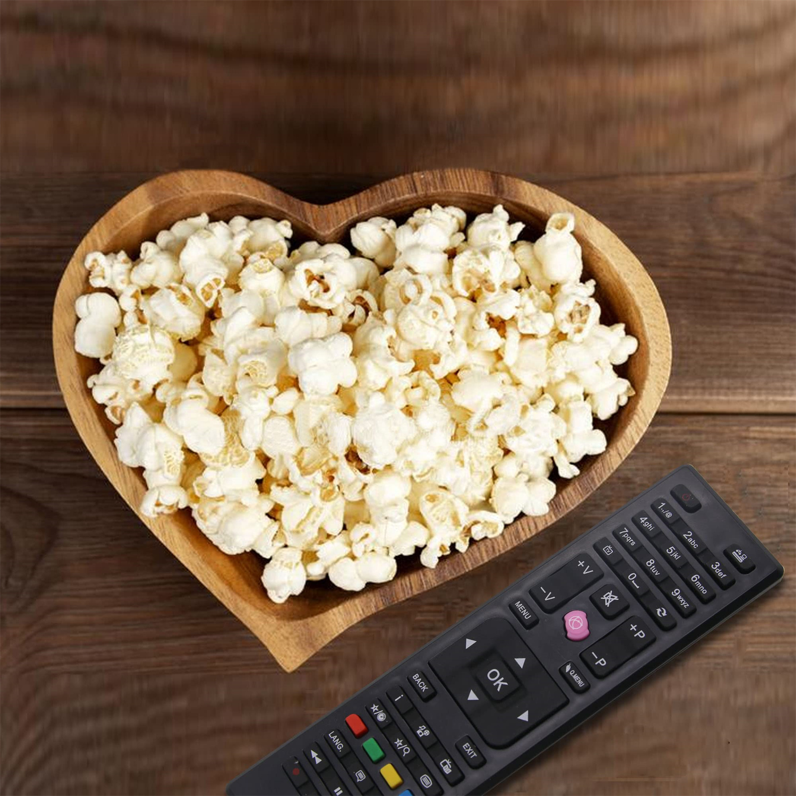 Holzschale in Herzform mit Popcorn und einer Fernbedienung auf einem Holztisch.