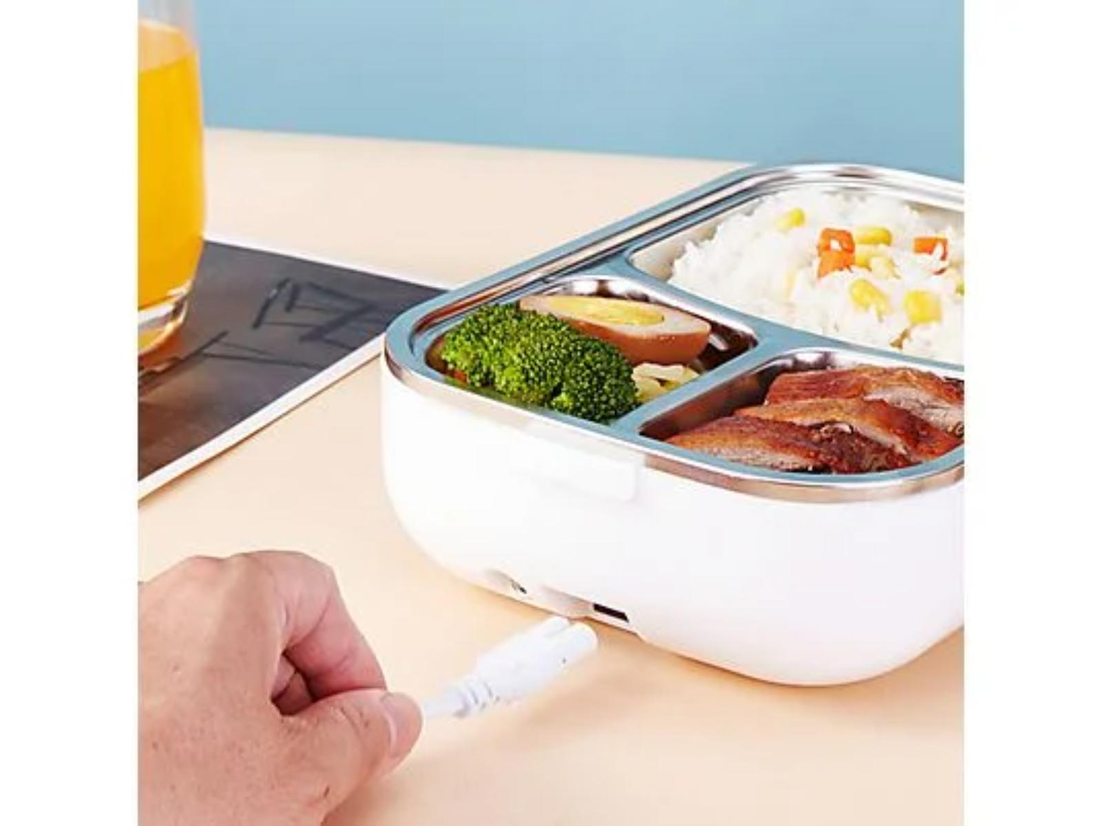 Eine Hand, die ein weißes Kabel in eine weiße Lunchbox mit Essen steckt. Orangensaft ist im Hintergrund.