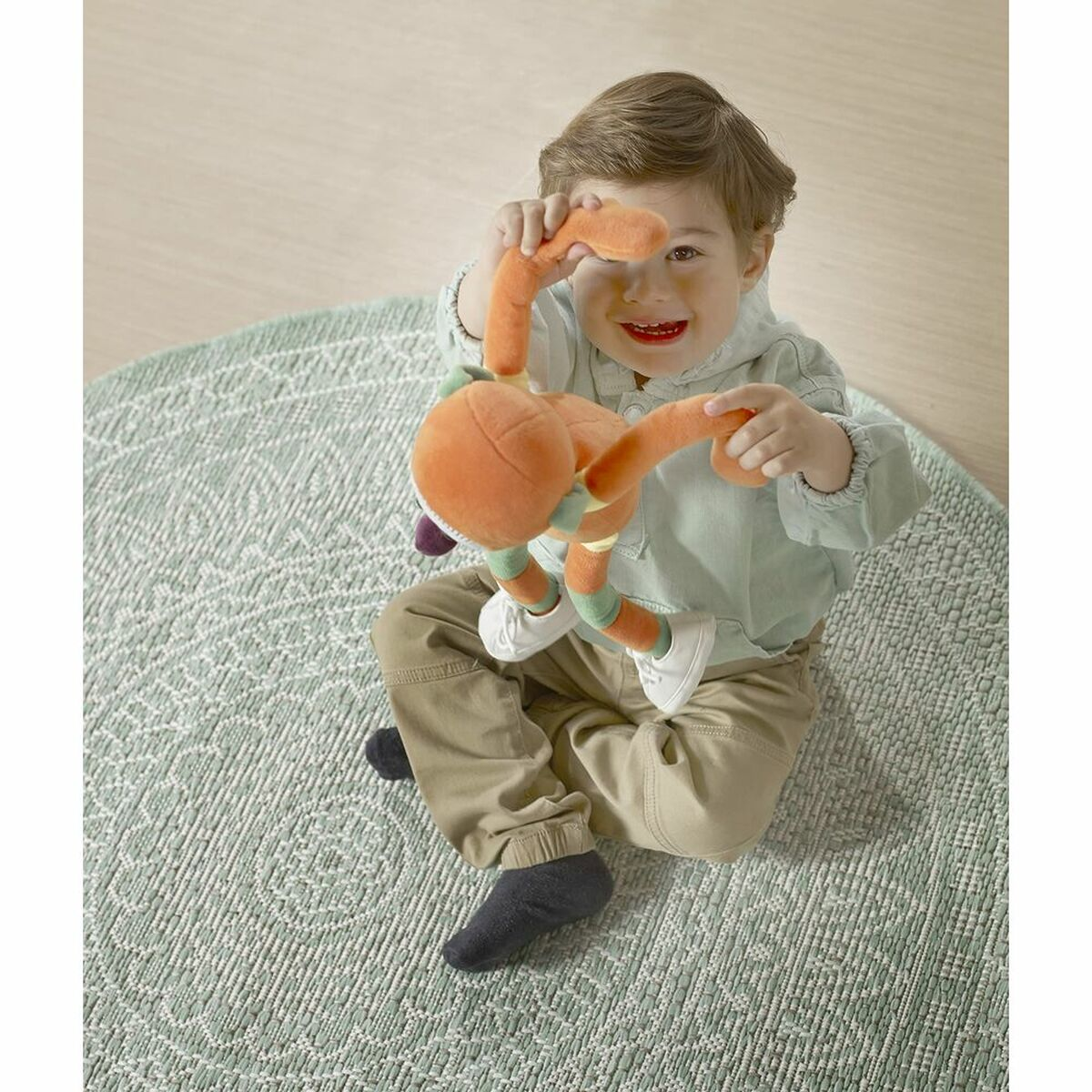 Małe dziecko siedzi na dywanie, trzymając pomarańczową pluszową zabawkę.